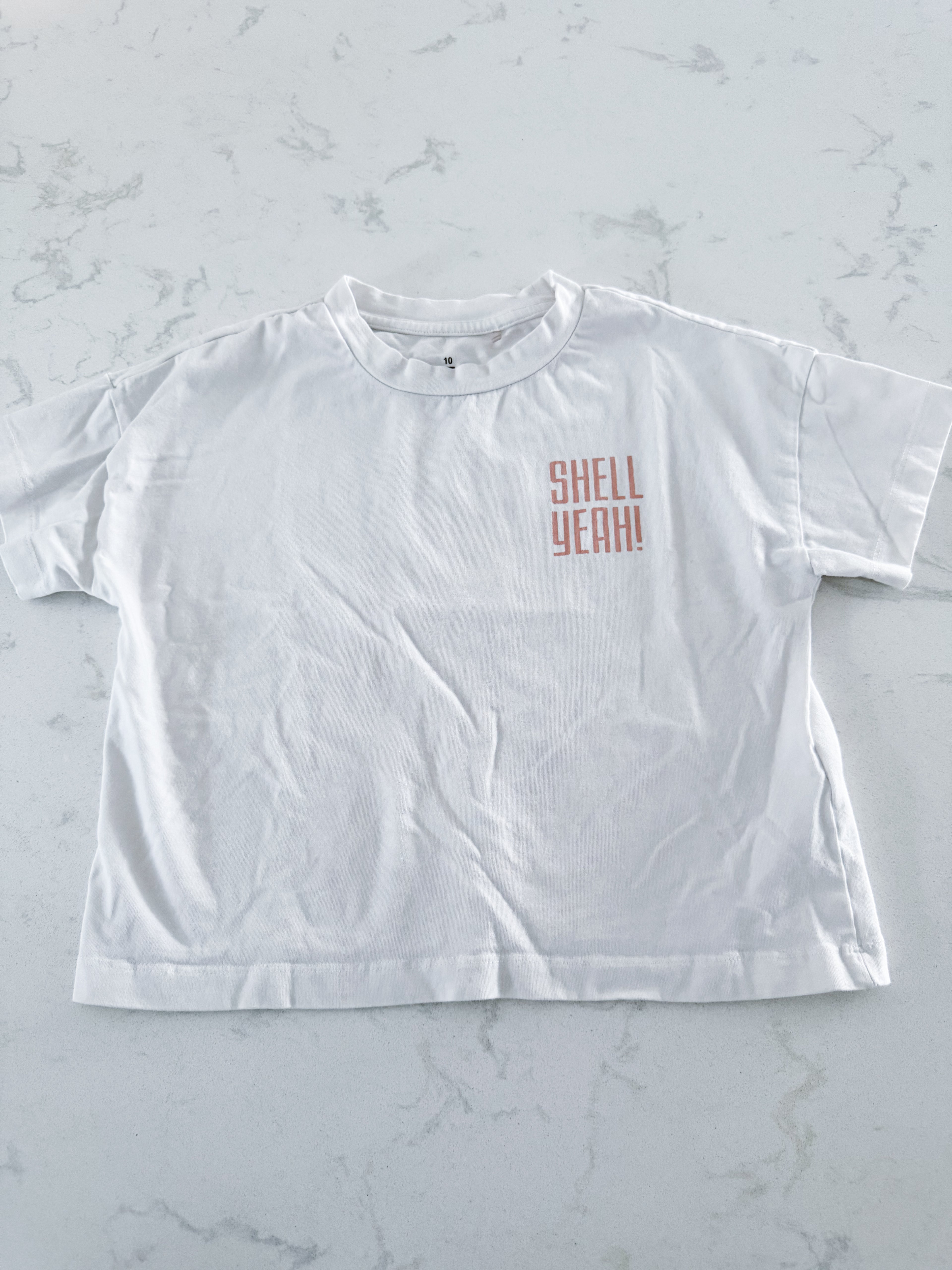 Tag- 10Y- VGUC- white short sleeve t shirt with “shell yeah” in beige