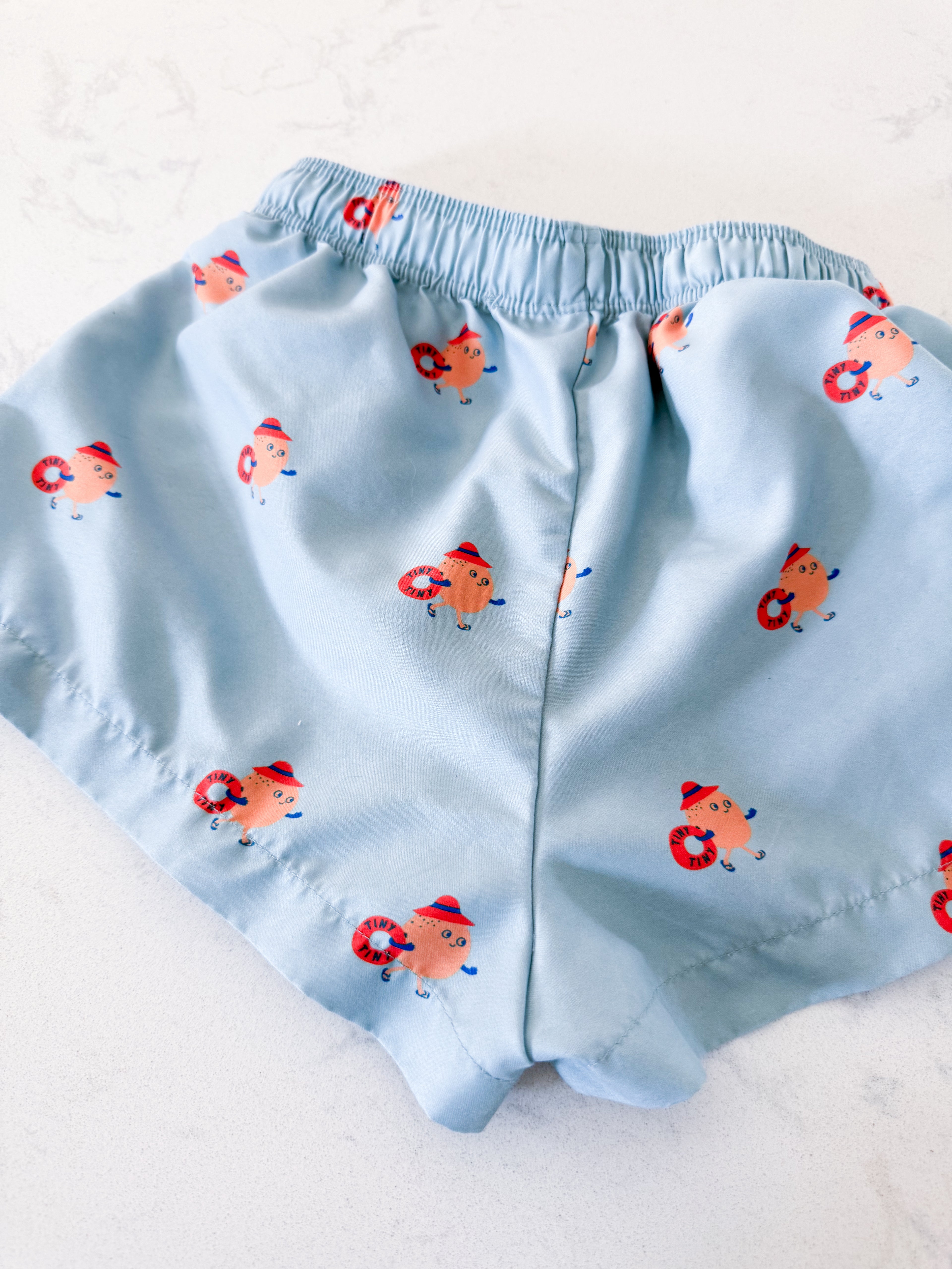 Tiny Cottons- fits 5T- VGUC- light blue swim trunks with orange cartoon graphic