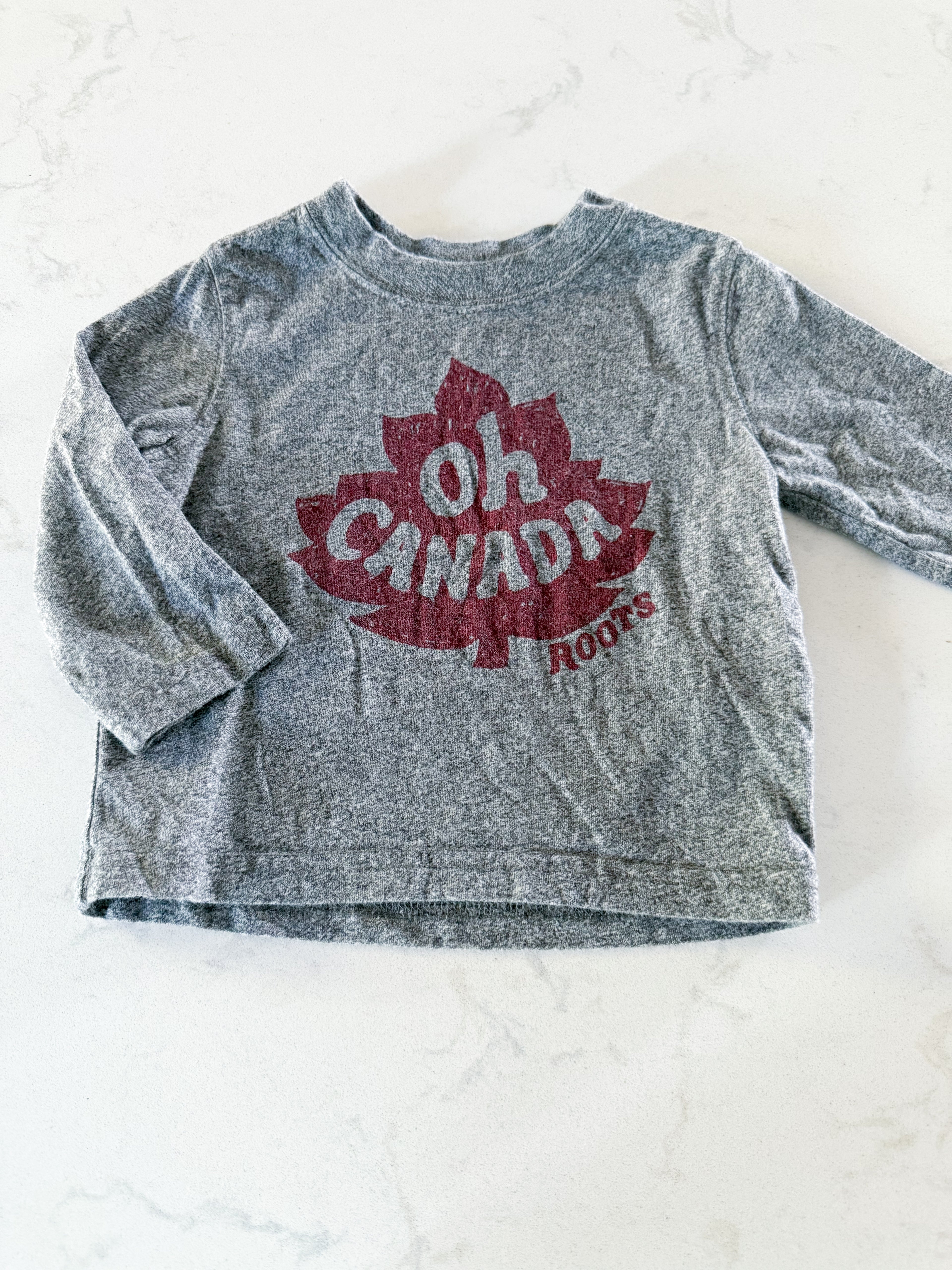 Roots- 6-12m- GUC- long sleeve grey shirt with maple leaf and “oh Canada” on front